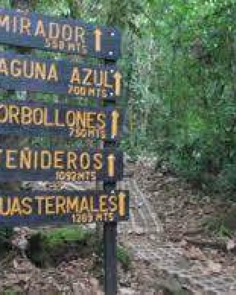 A weathered wooden sign with yellow text on a dark background, listing several locations including Laguna Azul.