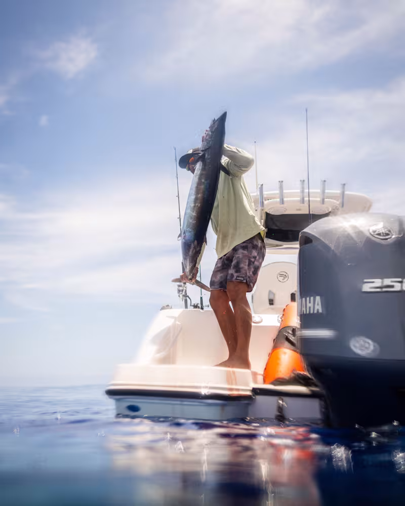 A smiling angler holding a large yellowfin tuna on a fishing boat.