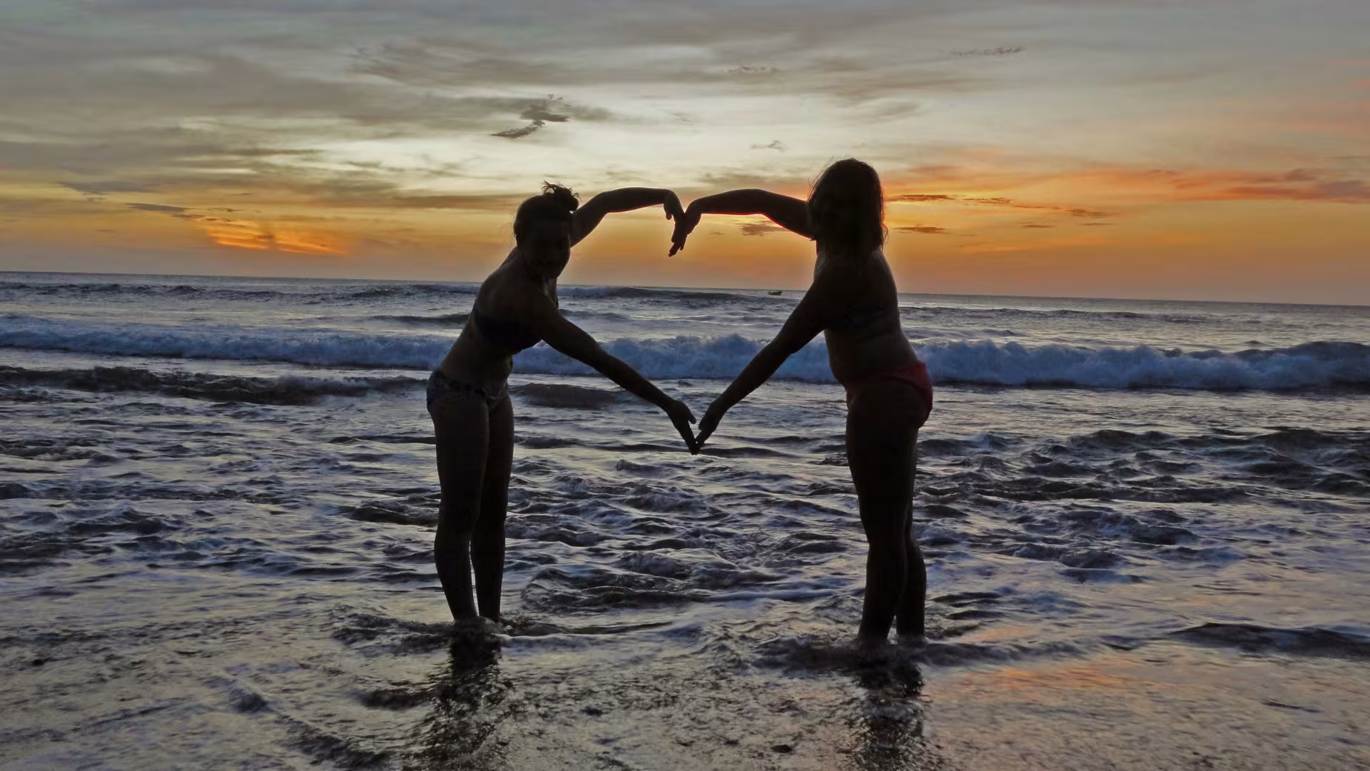 A couple on the beach touching hands to create a heart symbol